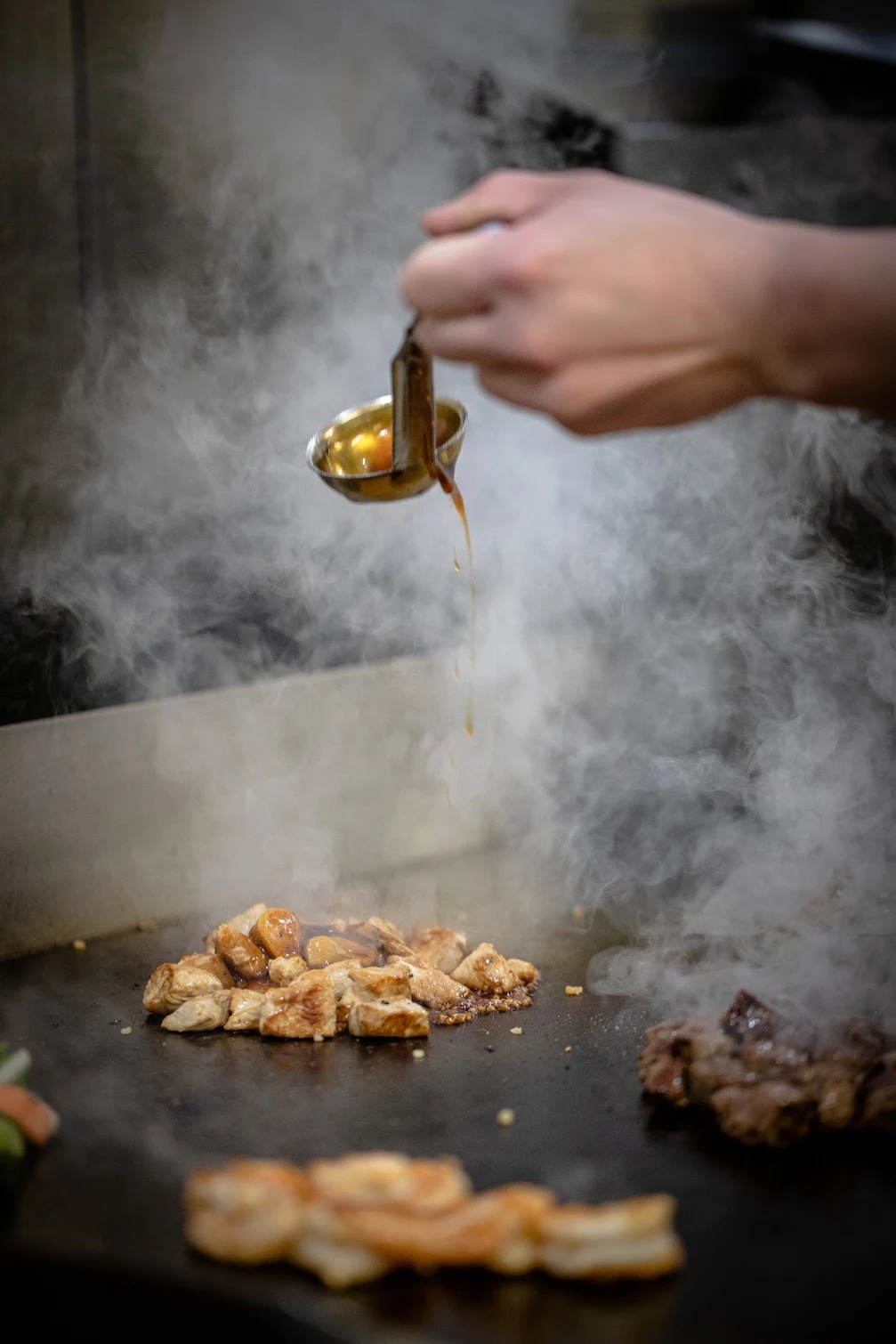 Sauce being poured over chicken on Kirin’s steaming hibachi grill